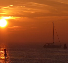 Orange-gelber Sonnenuntergang über dem Meer. Segelboot als Schatten erkennbar